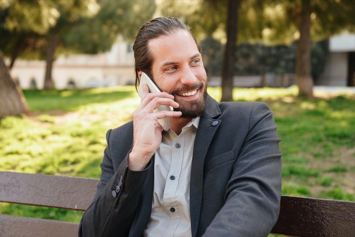 בעל עסק מחייך ומדבר בטלפון בחוץ — לקוח ג'ינגלפון מרוצה